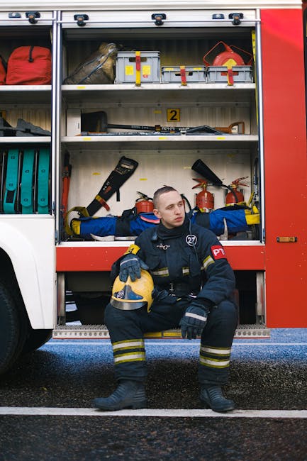 Firefighter in uniform sits next to a well-equipped fire truck ready for emergency response.